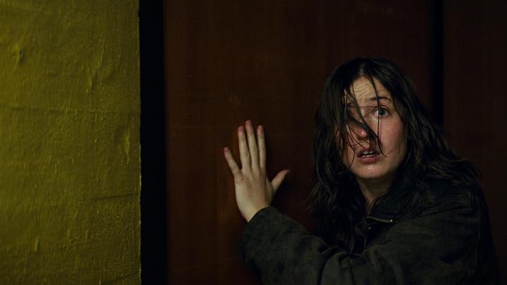 A frightened woman hides behind a door in Nightwatch Demons are Forever, emphasizing the film’s suspenseful tone.