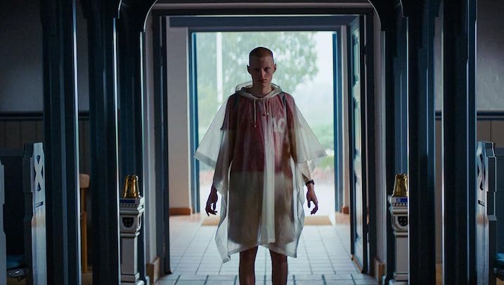 A teen wearing a translucent rain poncho stands ominously in a hallway in Nightwatch Demons are Forever.