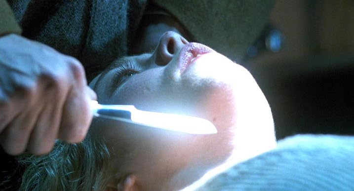 Terrifying close-up from Nightwatch (1994) showing a sharp blade held to a woman’s throat under stark white lighting.