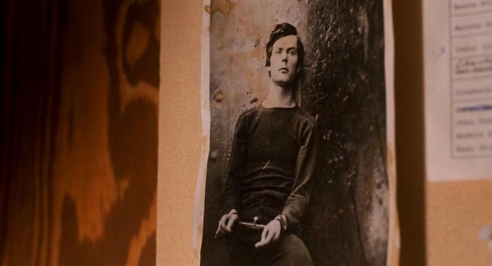 Old black-and-white photo of a man in handcuffs pinned to a bulletin board, hinting at past crimes in Nightwatch (1994).
