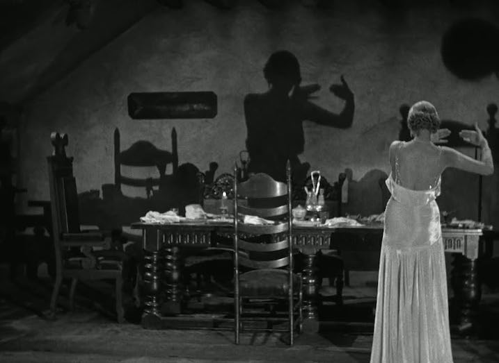  Scene from The Old Dark House (1932) featuring a woman in a satin gown casting playful hand shadows on the wall of a dimly lit dining room. Evokes German Expressionist influences.