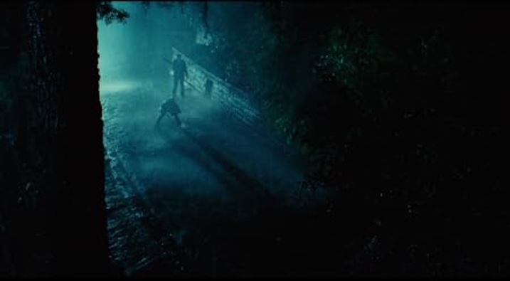 Two silhouetted figures square off under a rain-drenched streetlamp in a forested alley. Heavy shadows and cool blue-green lighting create a moody, noir atmosphere.