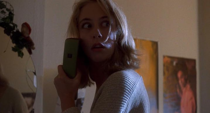 A frightened woman holding a green cordless phone, looking toward something off-screen in a tense moment from Nightwatch (1994).