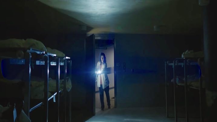A character explores a morgue with a flashlight in Nightwatch Demons are Forever, highlighting the film’s atmospheric horror setting.