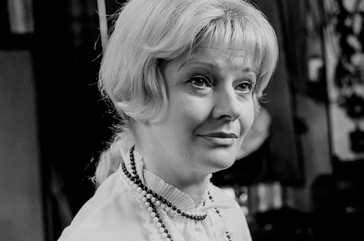 Black-and-white still of an older woman in pearls and a white blouse, promotional image not taken from the Blu-ray.