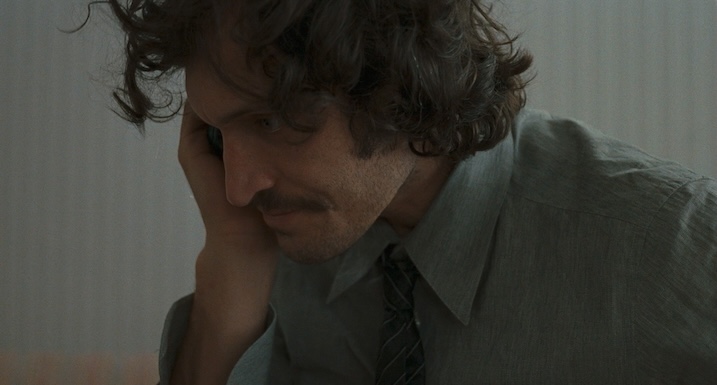 Vincent Gallo as Shane Brown in Trouble Every Day, holding a phone to his ear in a muted, dimly lit scene.
