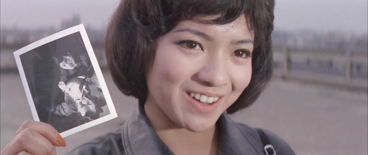 Close-up of female character: “Chieko Matsubara smiling while holding a photo in Black Tight Killers (1966), showcasing her key role in the Japanese spy caper.”