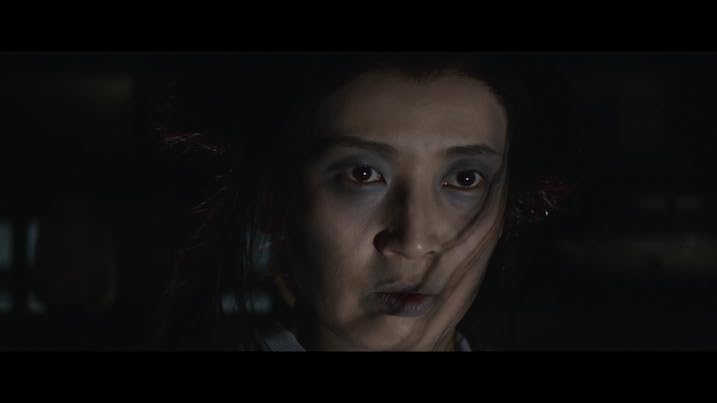 Close-up of Miyoko Akaza as Otsuyu in The Bride from Hades – ghostly makeup and hair accessories, lit dramatically in a darkened setting.