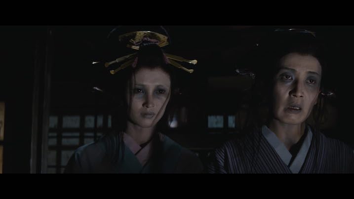 Miyoko Akaza and co-star in The Bride from Hades – both in traditional attire with pale, haunting makeup, framed in a shadowy interior.