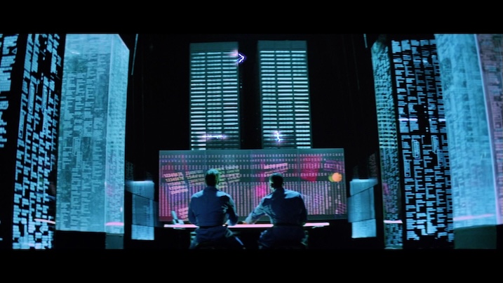 Hackers (1995) computer visualization scene – stylized cyberspace with glowing neon towers and massive data screens.