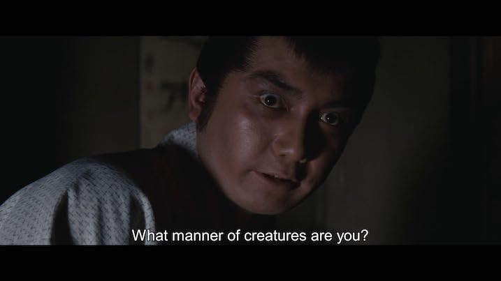Kojiro Hongo in The Bride from Hades – intense expression with English subtitle text “What manner of creatures are you?” over a dimly lit background.