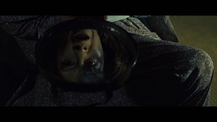 Scene from The Ghost of Yotsuya (1959) – Upside-down reflection of a woman’s ghostly face in a handheld mirror, illuminated in eerie greenish light.