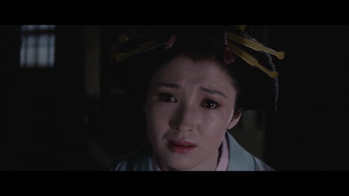 Miyoko Akaza as Otsuyu in The Bride from Hades – close-up showing tearful expression and elaborate hairpins, framed by darkness.