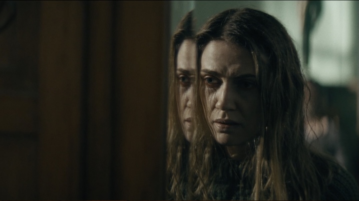 Image 1: Sara Canning’s character stares anxiously into a mirror in Shaman (2025), her reflection emphasizing the film’s psychological tension.